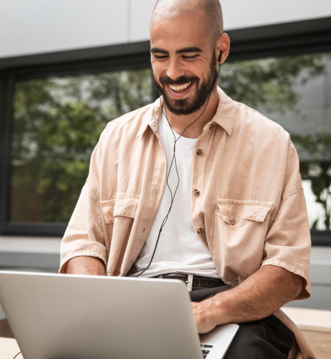 Imagem de um homem sentado, olhando um laptop e sorrindo.